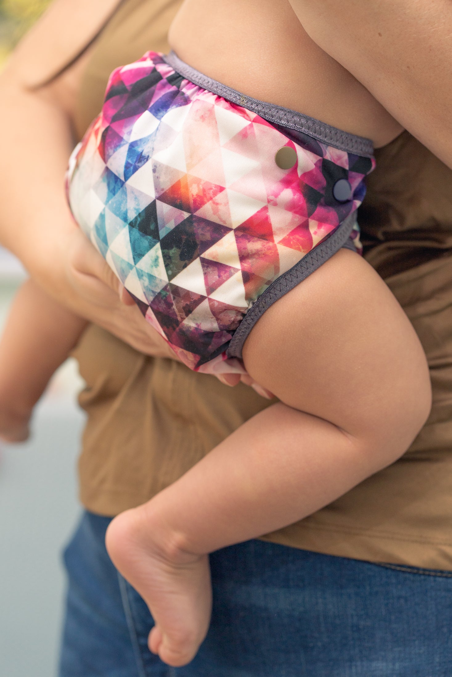 Baby auf dem Arm trägt eine bunte Stoffwindel mit Dreieckmuster